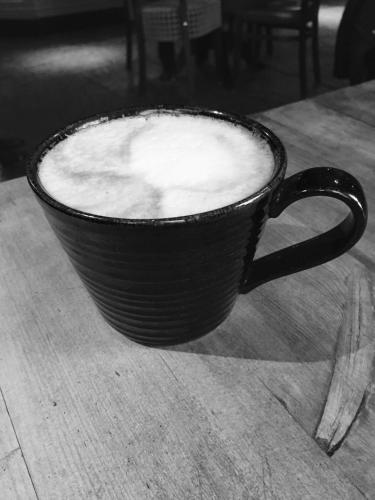 a black coffee cup sitting on a wooden table at Tilted Wig in Warwick