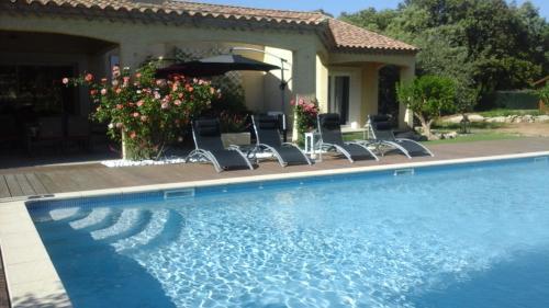 a pool with chairs and an umbrella next to a house at B&B Le Mas Des Chenes in Vacquières
