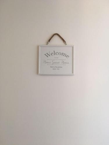 a sign that reads welcome hangs on a white wall at Blue Sky Apartments in Capo dʼOrlando