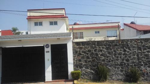 a white house with black doors and a stone wall at Casa privada para descanso, se renta para 8 personas completa Y tambien por habitacion con baño privado para 2 o 4 personas compartiendo areas comunes in Cuernavaca