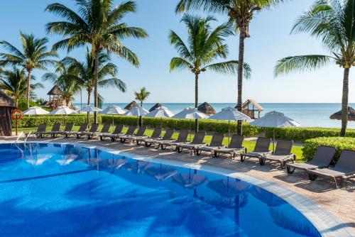 a pool with chairs and palm trees and the ocean at Ocean Coral & Turquesa All Inclusive in Puerto Morelos