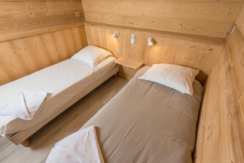 two beds in a room with wooden walls at Hôtel Flor'Alpes in La Giettaz