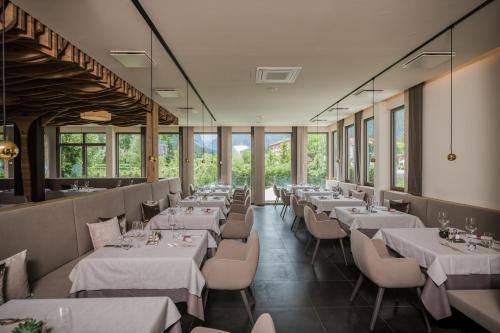 un restaurant avec des tables blanches, des chaises et des fenêtres dans l'établissement Park Hotel Bellevue, à Dobbiaco