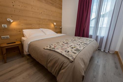 a bedroom with a bed with a wooden wall at Hôtel Flor'Alpes in La Giettaz
