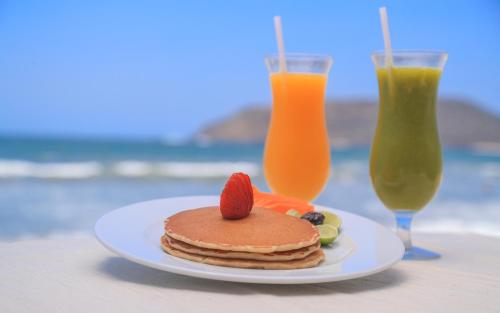 a plate of pancakes with a strawberry on top and two drinks at The Inn at Mazatlan in Mazatlán