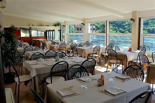 Un restaurante con mesas y sillas blancas y ventanas. en Appartamenti Tra gli Ulivi, en Bardino Nuovo