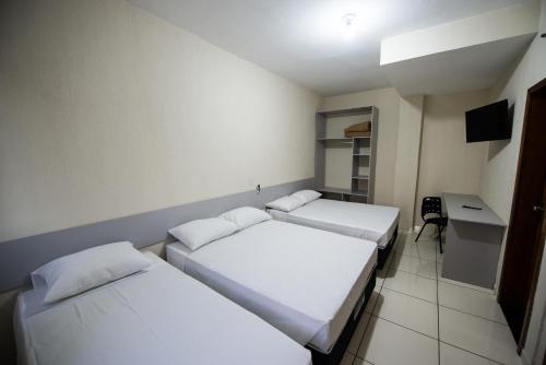 two beds in a room with a desk and a computer at Vila Dumont no Centro de Foz in Foz do Iguaçu