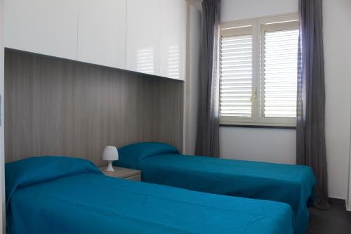 2 camas azules en una habitación con ventana en The Green Seaside en Fondachello
