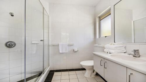 Baño blanco con aseo y lavamanos en Park Cove Apartments, en Noosa Heads