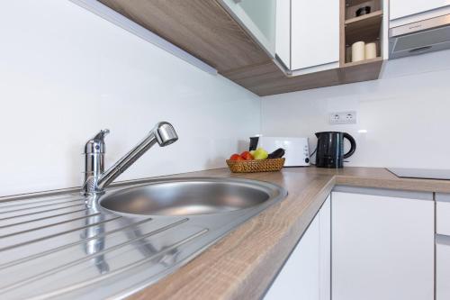 um lavatório de aço inoxidável numa cozinha com armários brancos em Apartments Niko em Malinska