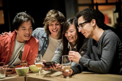 a group of people sitting at a table looking at a cell phone at HI Brussels Jacques Brel Hostel in Brussels