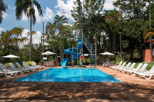 a swimming pool with a blue slide next to chairs at Hotel Fazenda Santa Monica in Louveira