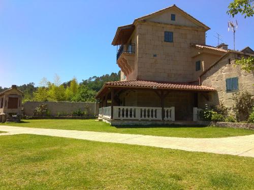 une grande maison en pierre avec une terrasse couverte sur une pelouse dans l'établissement La Torre Mondariz, à Mondariz
