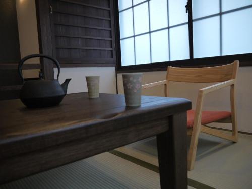 a table with two cups and a kettle and a chair at Machiya Kaemon in Kyoto