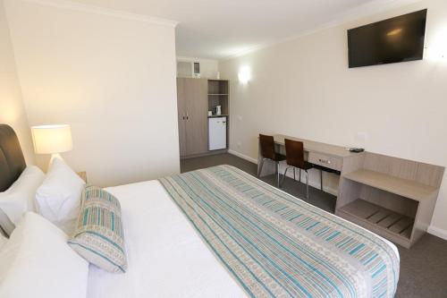 1 dormitorio con 1 cama y escritorio con TV en Seven Pines Motor Inn, en Mildura