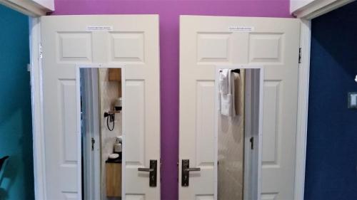 two white doors in a room with a purple wall at Bailey's Bed and Breakfast in Runaway Bay
