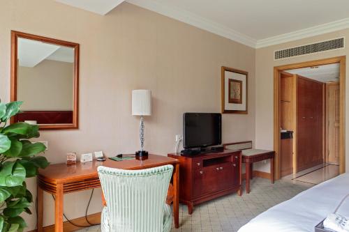 a hotel room with a bed and a desk with a television at Hong Qiao State Guest House in Shanghai