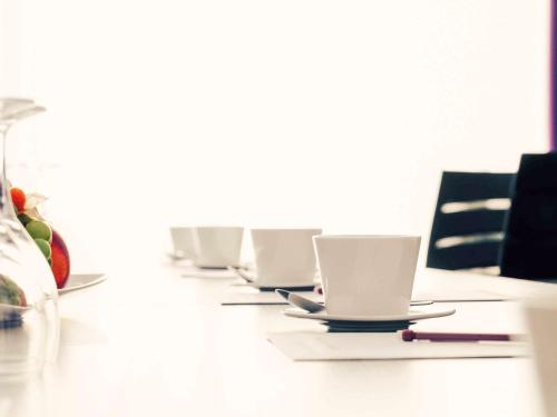a row of white cups and saucers on a table at Mercure Hotel Hagen in Hagen