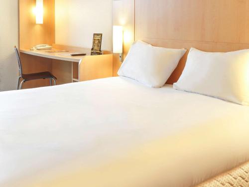 a large white bed with two pillows and a desk at ibis Etampes in Étampes