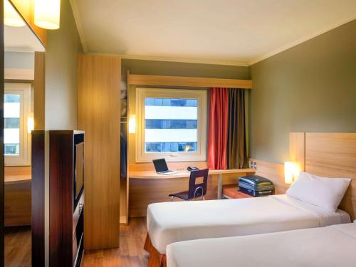 a hotel room with two beds and a desk with a laptop at ibis Santiago Las Condes in Santiago