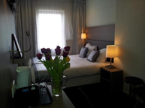 a bedroom with a bed with a vase of flowers on a table at The Concert Hotel in Amsterdam