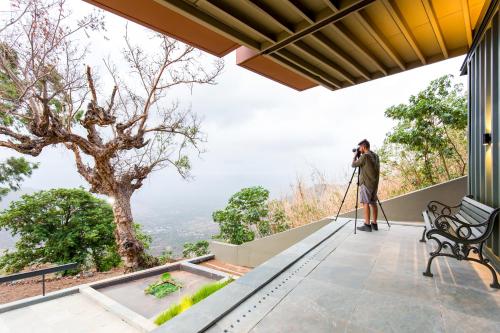 a man taking a picture of the view from a house at Zostel Plus Panchgani in Panchgani