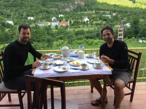 Zwei Männer sitzen an einem Tisch mit Essen drauf. in der Unterkunft Bujtina Kometa in Theth