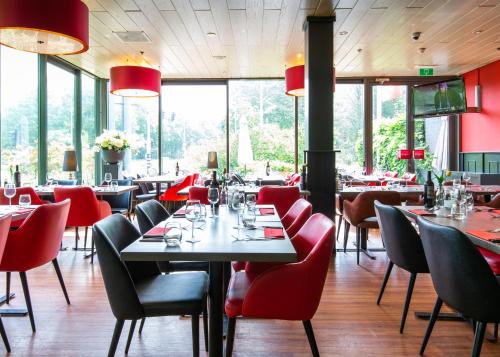 um restaurante com cadeiras vermelhas, mesas e janelas em Bastion Hotel Amsterdam Noord em Amesterdão