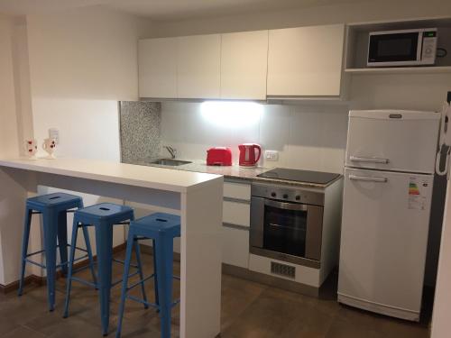 una cocina con armarios blancos y taburetes azules en Departamento moderno en Rosario