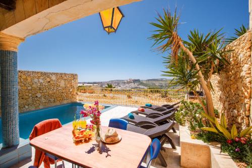un patio con mesa, sillas y piscina en Bellavista Farmhouses Gozo, en Xagħra