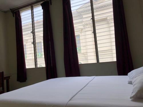 a bedroom with two windows and a bed with white sheets at Hotel El Palacio in San Salvador