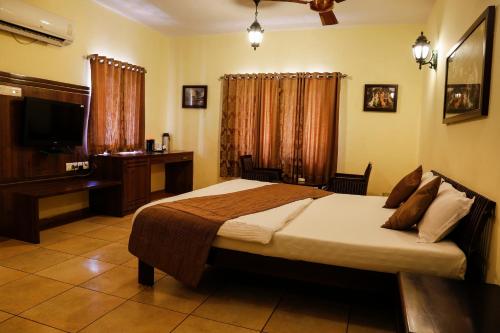a bedroom with a bed and a desk and a television at The Colonial Manek Manor By SAH in Mount Ābu