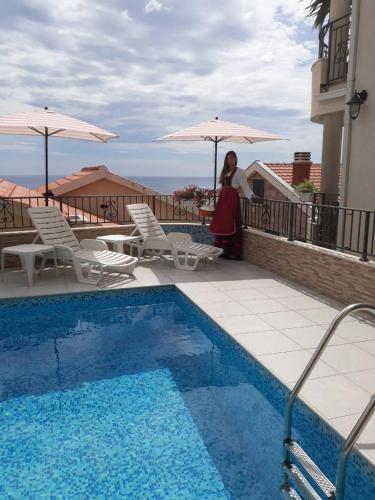 a woman sitting on a balcony next to a swimming pool at Apartments Leut in Sveti Stefan