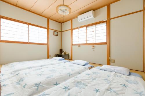 two beds in a room with two windows at A&Z Guest House in Kaizuka