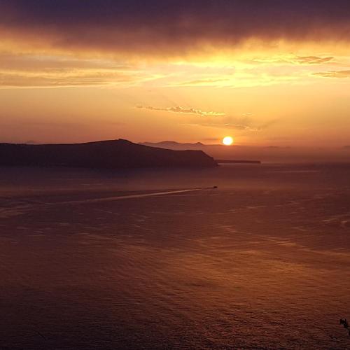 a sunset over the ocean with the sun in the sky at Adamant Suites in Fira