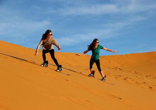 two women are skiing down a sand hill at Luxurious Merzouga Desert Camps in Merzouga