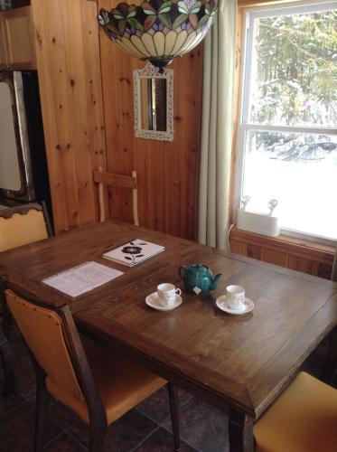 une table en bois avec des tasses et des soucoupes ainsi qu'une fenêtre dans l'établissement Chalet d'Anna, à Saint-Damien