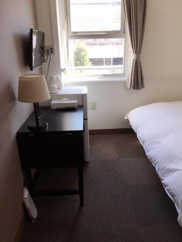a bedroom with a desk with a bed and a window at Business Hotel TenTen in Okayama