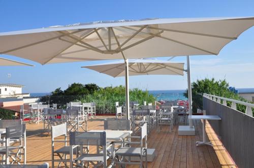 un patio con mesas y sillas bajo sombrillas blancas en Hotel Intervallo, en Torre Lapillo