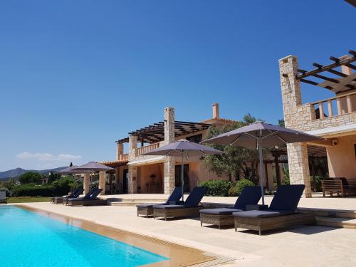 a pool with chairs and umbrellas next to a house at Therme Sea Luxury Lodge in Thermisia