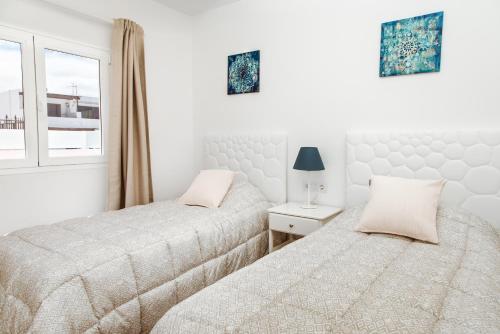 two beds in a white bedroom with a window at Apartamento Victoria in Puerto del Carmen