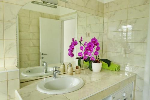 La salle de bains est pourvue d'un lavabo, d'un miroir et de fleurs violettes. dans l'établissement Apartments Curicta 1, à Krk