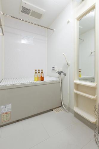 a white bathroom with bottles on a shelf at ABC Guest House 2F in Izumi-Sano