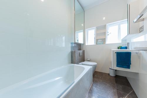 a white bathroom with a tub and a toilet at Beach Retreat in Sydney