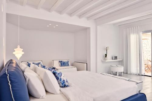 a white bedroom with a large bed with blue and white pillows at Katikies Mykonos - The Leading Hotels of the World in Agios Ioannis Mykonos