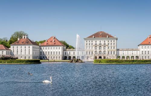 un cigno che nuota nell'acqua di fronte agli edifici di Laimer Hof am Schloss Nymphenburg a Monaco