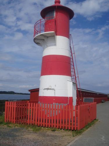 a red and white lighthouse behind a red fence at Strandhuset Holiday Home in Glyngøre