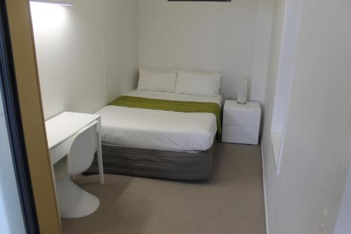 a small white bedroom with a bed and a desk at MCentral Apartments Manukau in Auckland