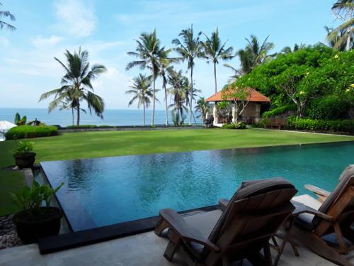 a pool with two chairs and the ocean in the background at Villa Rumah Pantai Bali in Selemadeg