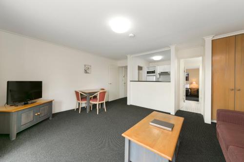 a living room with a couch and a tv and a table at Mt Ommaney Hotel Apartments in Brisbane